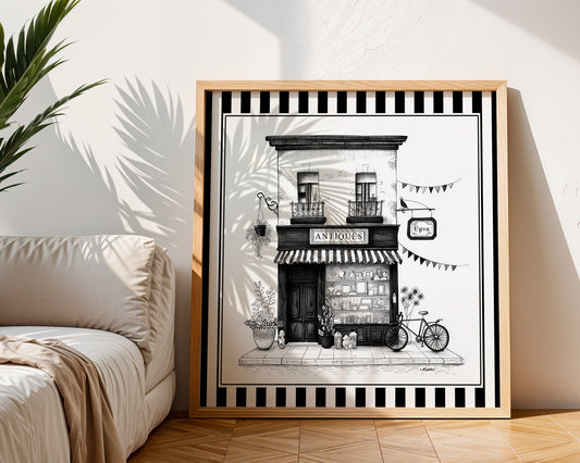 Black and white antique shop print displayed in a light wood square frame beside a neutral sofa