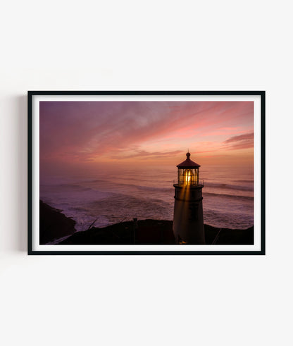 Bring calm coastal atmosphere to your space with this lighthouse sunset print, featuring a glowing beacon, soft ocean waves, dramatic shoreline and warm pink evening sky for bathrooms, bedrooms, living rooms, offices, beach houses and gallery walls.
