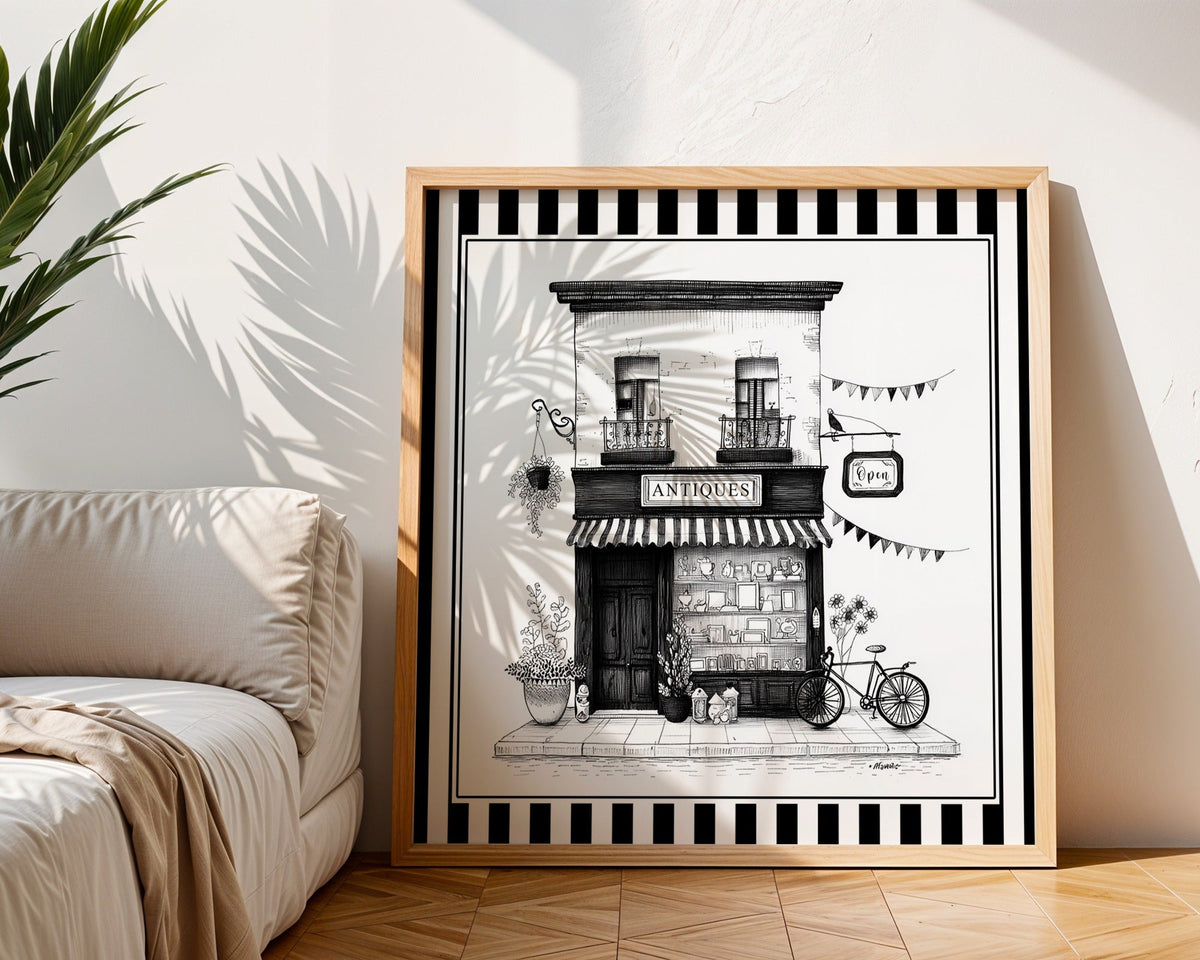 Black and white antique shop print displayed in a light wood square frame beside a neutral sofa
