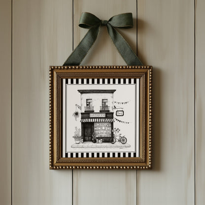Black and white antique shop print displayed in an ornate gold square frame with ribbon