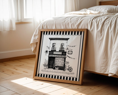 Black and white antique shop print displayed beside a bed in a light wood square frame