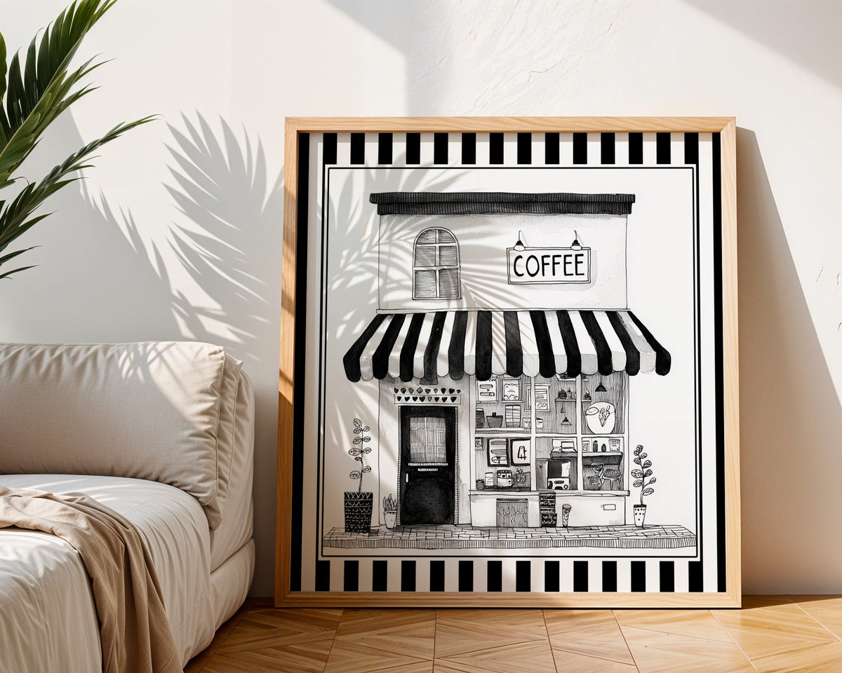 Black and white coffee shop print displayed in a light wood square frame beside a neutral sofa