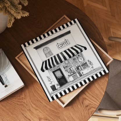 Square black and white coffee shop print displayed flat on a wooden table