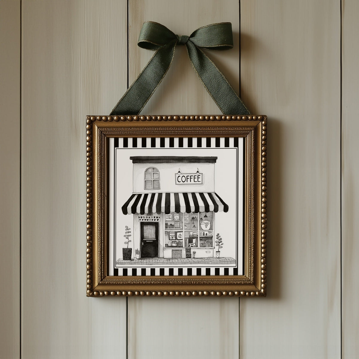 Black and white coffee shop print displayed in an ornate gold square frame with ribbon