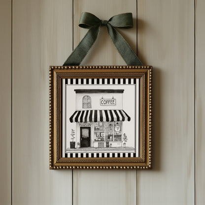Black and white coffee shop print displayed in an ornate gold square frame with ribbon