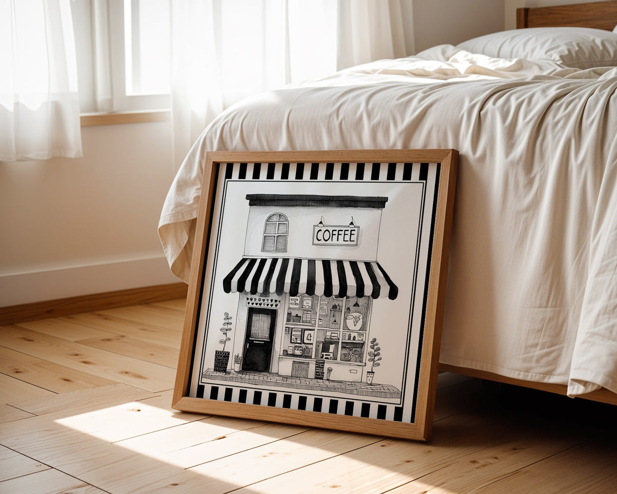 Black and white coffee shop print displayed beside a bed in a light wood square frame
