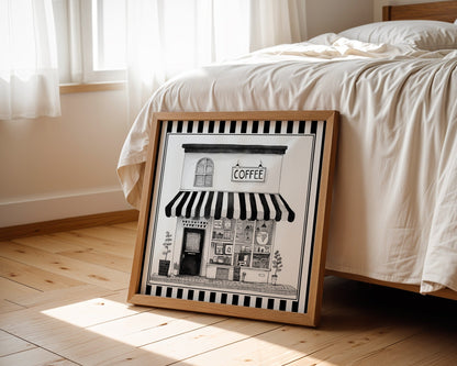 Black and white coffee shop print displayed beside a bed in a light wood square frame