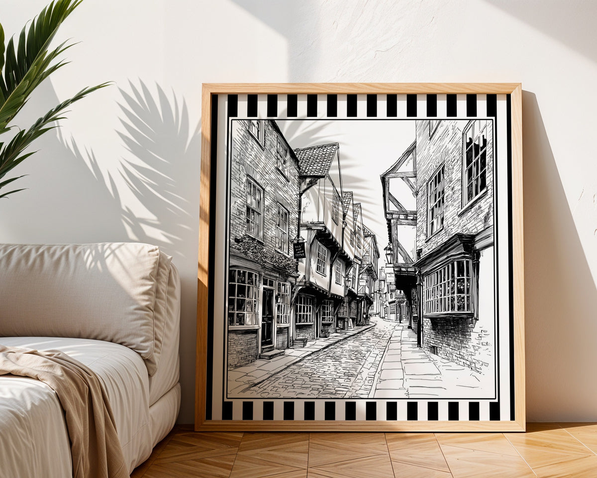 Black and white York Shambles street line art displayed in a light wood square frame beside a neutral sofa