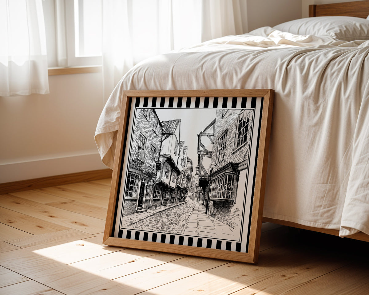 Black and white York Shambles street print displayed beside a bed in a light wood square frame