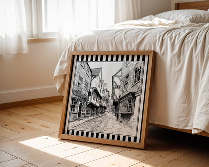 Black and white York Shambles street print displayed beside a bed in a light wood square frame